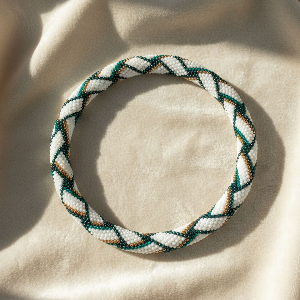 Collana artigianale Cupa Loom, realizzata con la tecnica del bead crochet, che unisce la lavorazione all’uncinetto alla tessitura di perline. Il motivo intrecciato crea un elegante effetto geometrico tridimensionale, esaltando il contrasto tra il bianco luminoso, il verde petrolio e i raffinati dettagli oro. Ogni collana è interamente realizzata a mano con perline giapponesi Toho, apprezzate per la loro precisione e qualità, e rifinita con una chiusura a scomparsa che mantiene la continuità e l’armonia del design.