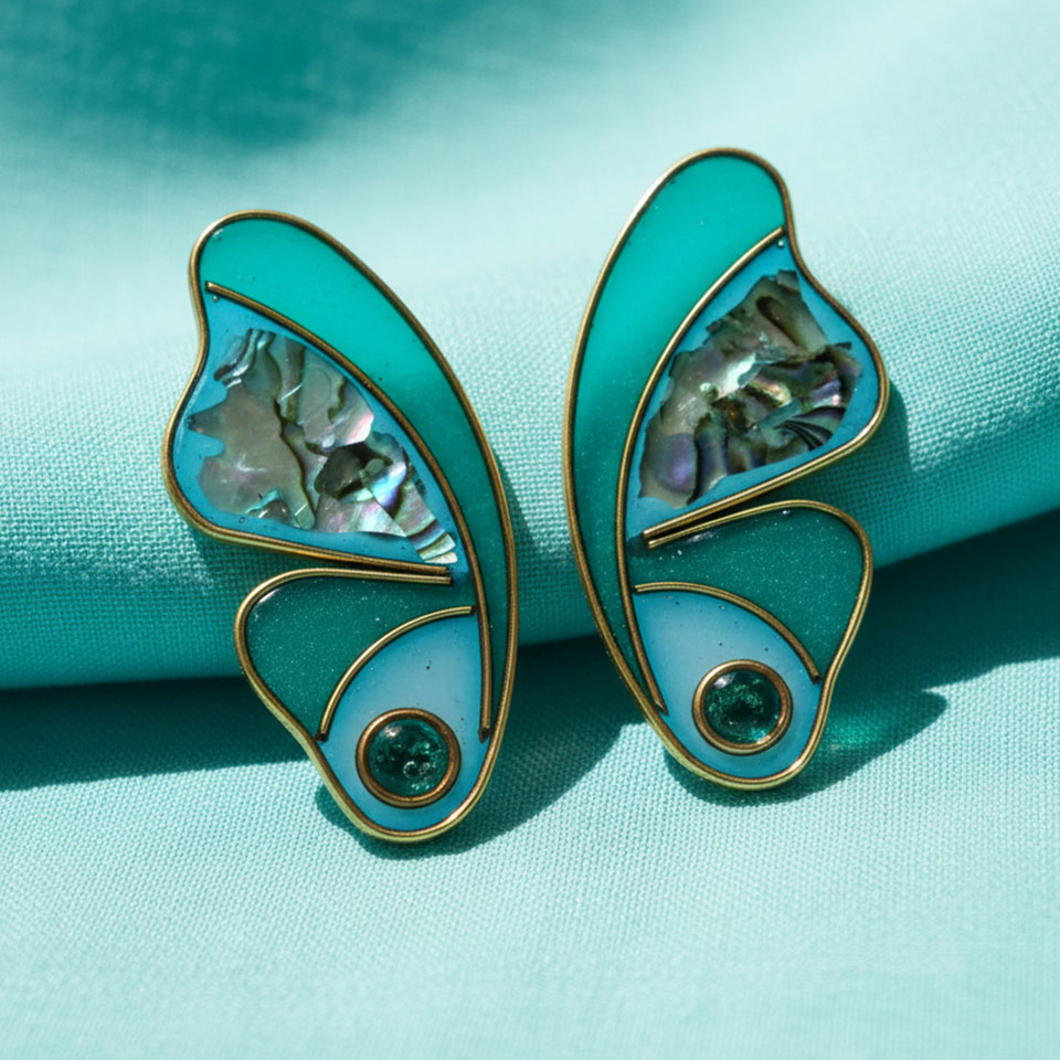 Freschi e luminosi come acque cristalline illuminate dal sole, gli orecchini CUPA TWIN BLUE evocano la magia dei riflessi marini. Le tonalità turchesi si fondono con la profondità cangiante della madreperla, creando giochi di luce sempre diversi, mentre le linee fluide e i dettagli dorati esaltano un’eleganza naturale. Un delicato punto luce completa il design con un tocco contemporaneo. Realizzati con cura in 4 ore di lavorazione, sono perfetti per chi ama colori vibranti ma raffinati, capaci di illuminare il viso con leggerezza e stile.