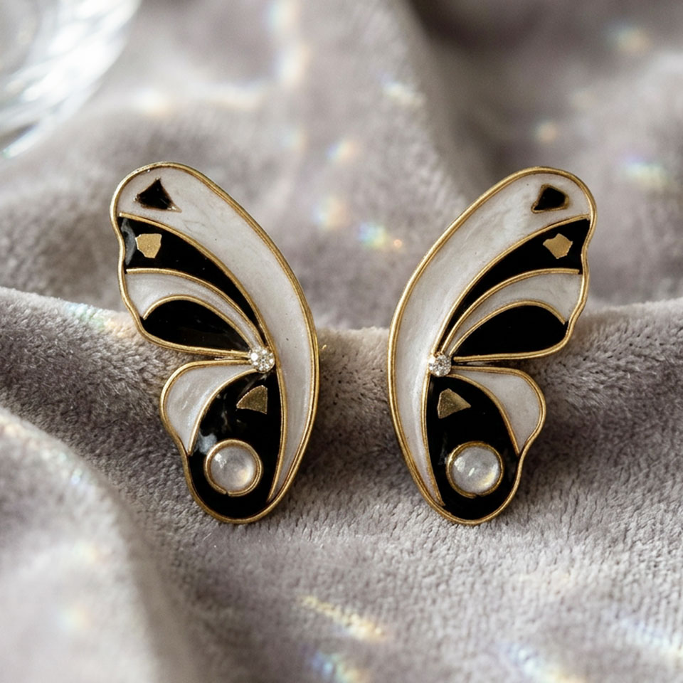 Gli orecchini Cupa Twin esprimono un perfetto equilibrio tra luce e ombra, con linee sinuose ispirate alla leggerezza delle ali. Il nero profondo si fonde con bagliori dorati in un design raffinato e magnetico, mentre piccoli riflessi luminosi donano carattere con discrezione. Leggerissimi e realizzati a mano come pezzo unico, presentano chiusura a perno e sono creati in resina e ottone con dettagli in vetro dorato, nel classico contrasto nero con inserti dorati. Perfetti per chi ama uno stile essenziale ma ricco di personalità, aggiungono un tocco di eleganza contemporanea capace di rendere unico anche il look più semplice.