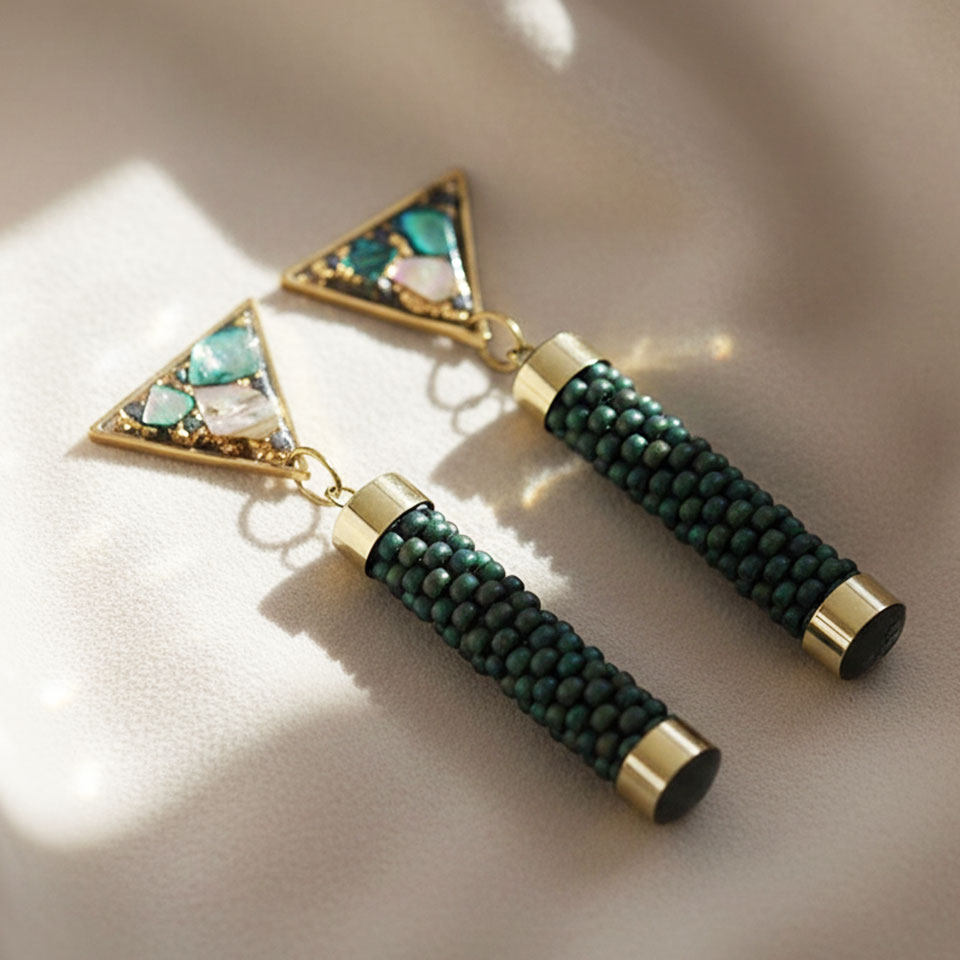 Gli orecchini Cupa Deep uniscono eleganza contemporanea e anima artigianale in un design geometrico raffinato. Il contrasto tra il cilindro in bead crochet e il triangolo luminoso crea un equilibrio armonioso tra texture e luce. Il triangolo in resina, realizzato a mano, racchiude frammenti iridescenti di madreperla con delicate inclusioni in foglia d’oro, mentre la parte cilindrica è tessuta con perline giapponesi Toho. Ogni paio richiede circa 7 ore di lavorazione artigianale.