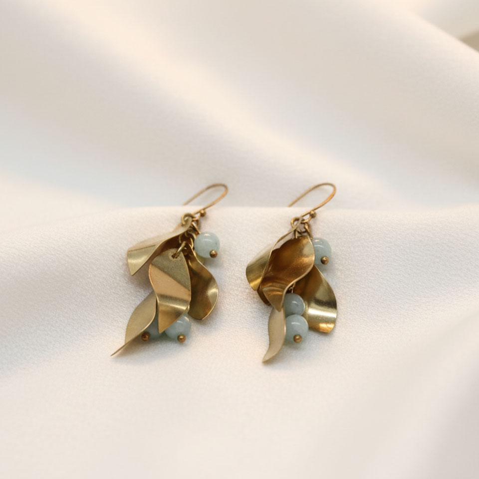 Questi orecchini prendono vita da un’attenta lavorazione artigianale durata oltre 5 ore, in cui ogni elemento in ottone è stato intagliato e modellato a mano singolarmente. I petali, luminosi e naturali, si intrecciano con delicate perline di calcedonio dalle sfumature azzurre, creando un equilibrio armonioso tra materia e luce. Un gioiello raffinato e poetico, pensato per esaltare con eleganza ogni movimento del viso.